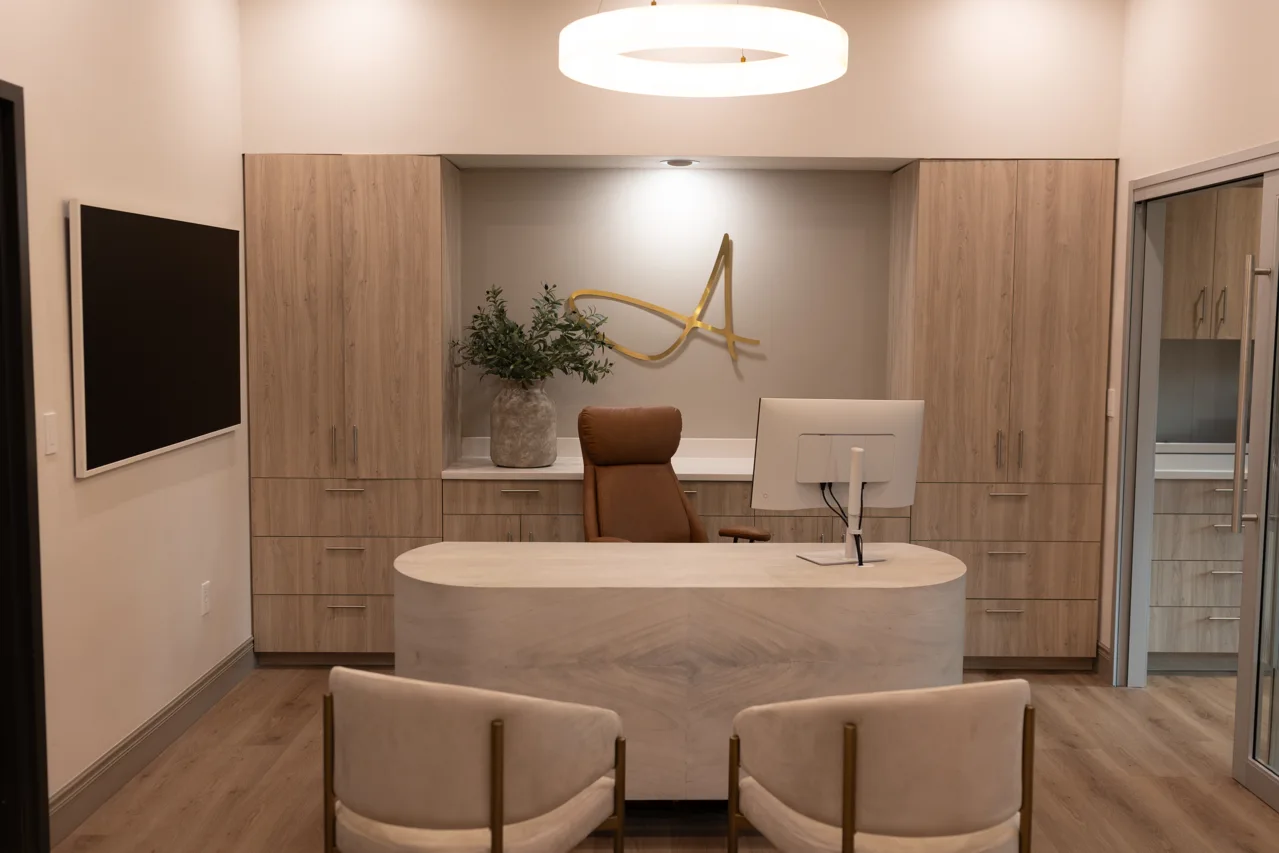 Consultation room with a desk, two guest chairs and the Alec Hall Esthetics wall mark
